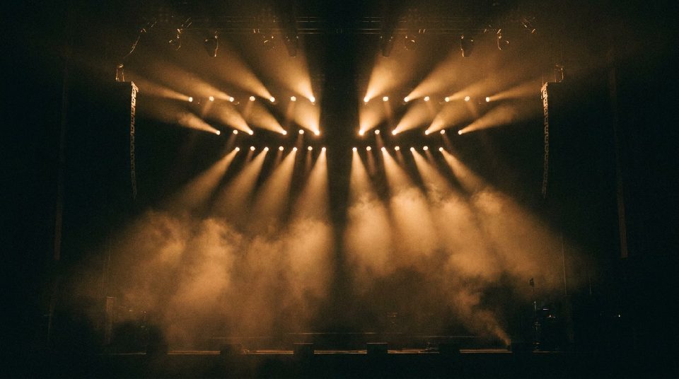 Rows of golden concert beams fanning through smoke over an empty stage